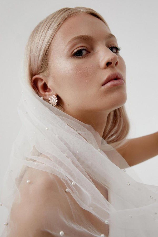 Long Wedding Veil with pearls draped over a bride's shoulder as she looks to the camera wearing a sparkling statement earring